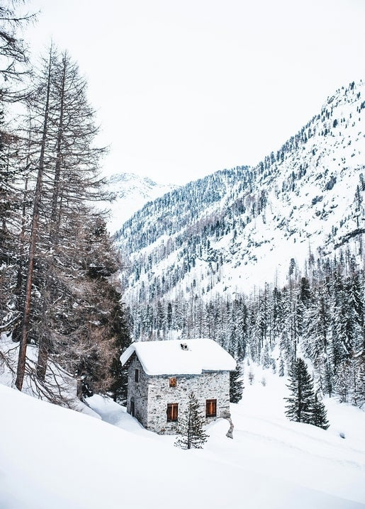 Snow-covered stone chalet in an alpine valley surrounded by pine trees