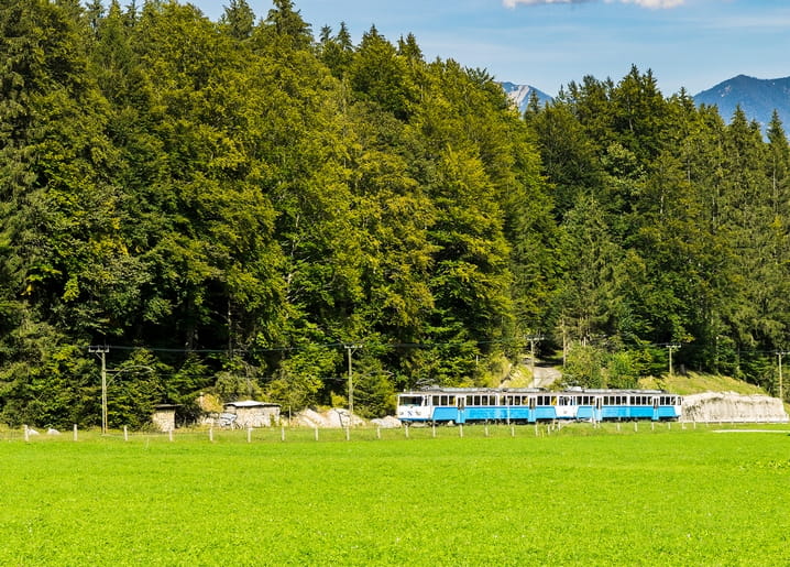 Blaue Bergbahn fährt am Nadelwald unterhalb der Alpen entlang