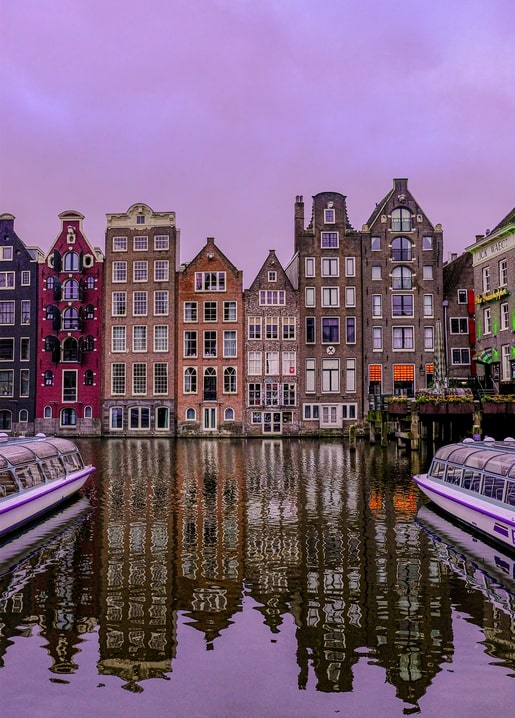 Amsterdam canal houses reflected in water at dusk with moored tour boats