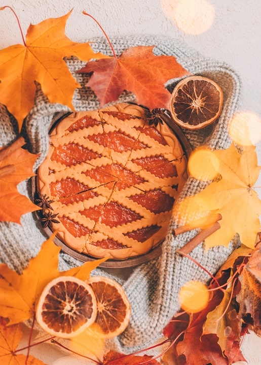 Kuchen mit Gitterkruste, Ahornblättern, getrockneten Orangenscheiben und Zimtstangen auf einer Wolldecke