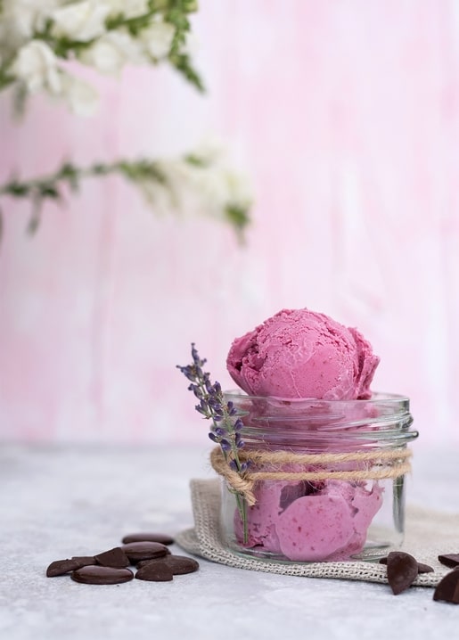 Kugel rosa Beereneis im Glas, verschnürt mit Lavendel, daneben Schokoladenherzen