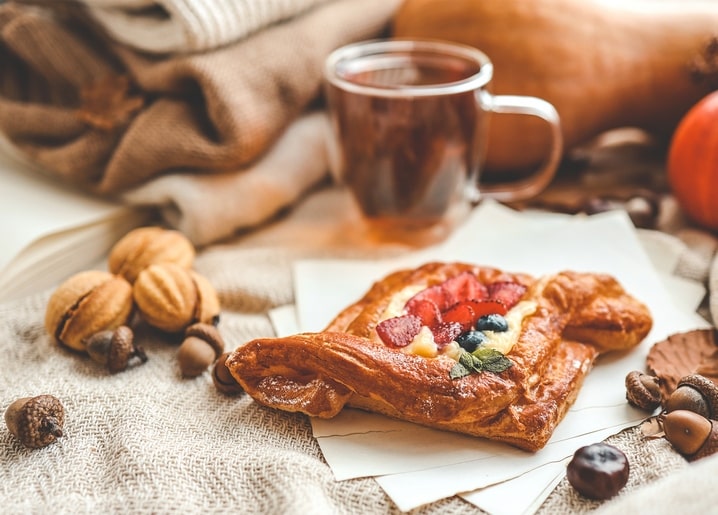 Blätterteig-Gebäck mit Erdbeeren und Blaubeeren neben einer Tasse Tee, Walnüssen, Eicheln und einem kleinen Kürbis