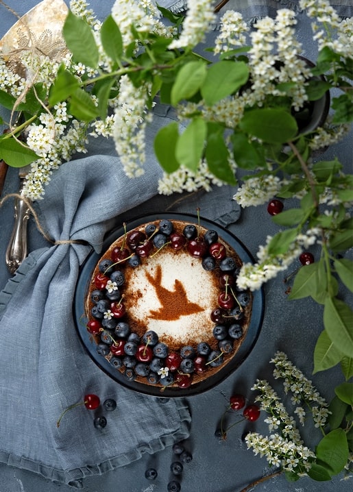 Beerentorte mit Zimt-Vogel-Muster, blauer Serviette und blühenden Zweigen