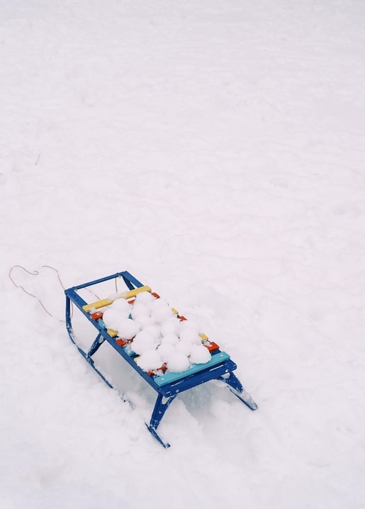 Blue wooden sled piled with hand-packed snowballs sitting alone in fresh snow