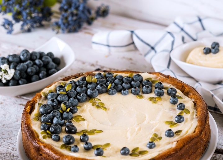 Blueberry cheesecake topped with pumpkin seeds beside a bowl of berries and dried lavender