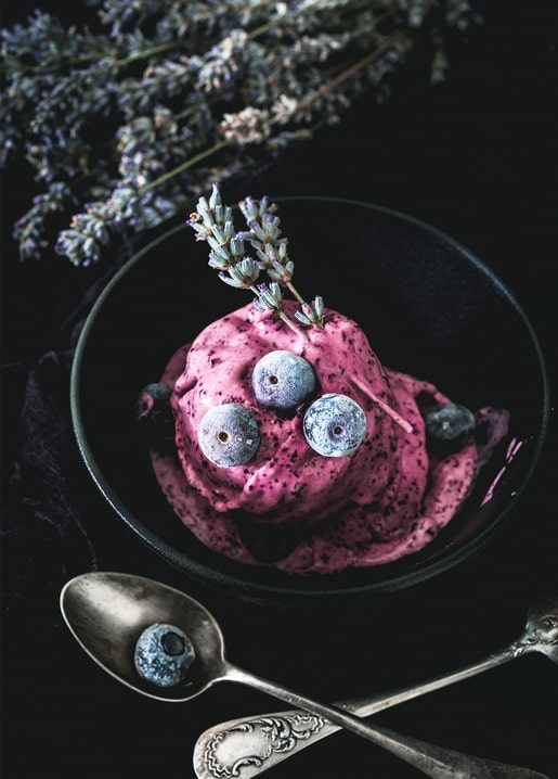 Blaubeer-Lavendel-Eis mit Beeren und Lavendel in dunkler Schale mit antiken Löffeln