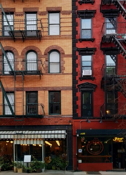 Row of brick and red apartment buildings with iron fire escapes and street-level shops