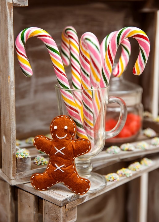 Striped candy canes in a glass mug beside a felt gingerbread man and sprinkled treats