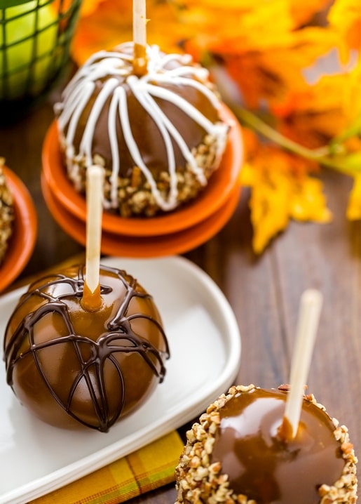 Karamelläpfel mit Schokoladenguss und gehackten Nüssen vor Herbstlaub