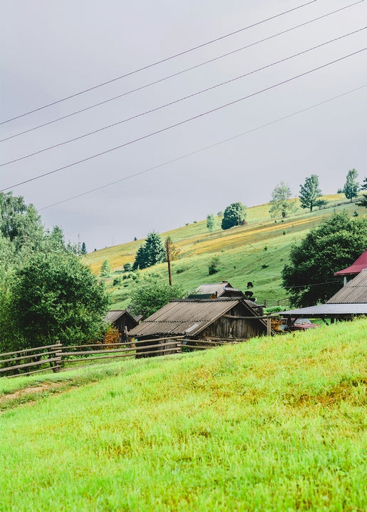 Wooden farmhouse and fence on a green Carpathian hillside under a cloudy sky