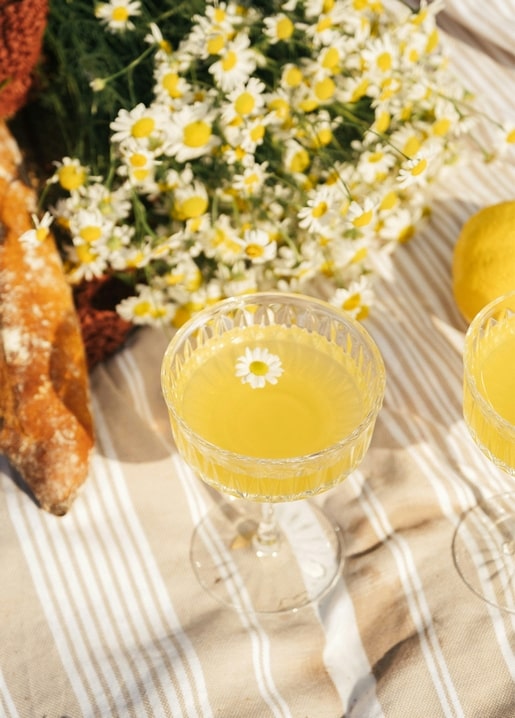 Kamillenblüte schwimmt im Limonadenglas neben Brot, Zitronen und einem Kamillenstrauß