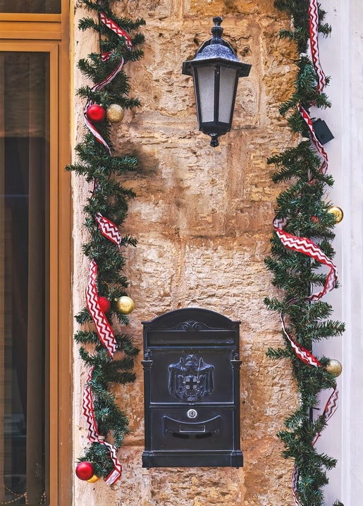 Black mailbox and lantern on a stone wall framed by pine garland and baubles