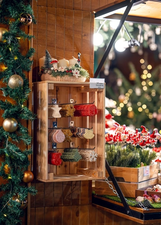 Handgeschnitzte Holzornamente in einer Kiste am Weihnachtsmarktstand mit Girlande und Lichtern