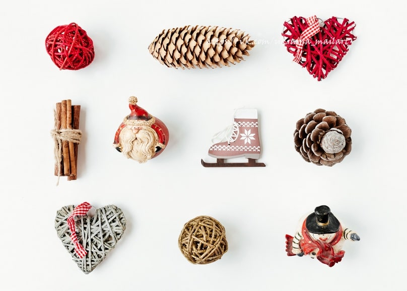 Flatlay mit Weihnachtsdeko: Rattanherz, Zapfen, Santa-Figur, Zimtstangen und gestrickter Schlittschuh