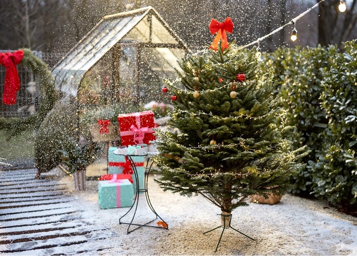 Decorated Christmas tree with fairy lights and gifts in a snowy garden