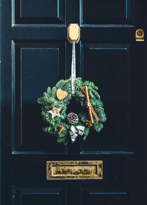 Fir wreath with cinnamon sticks and a gingerbread heart on a navy front door