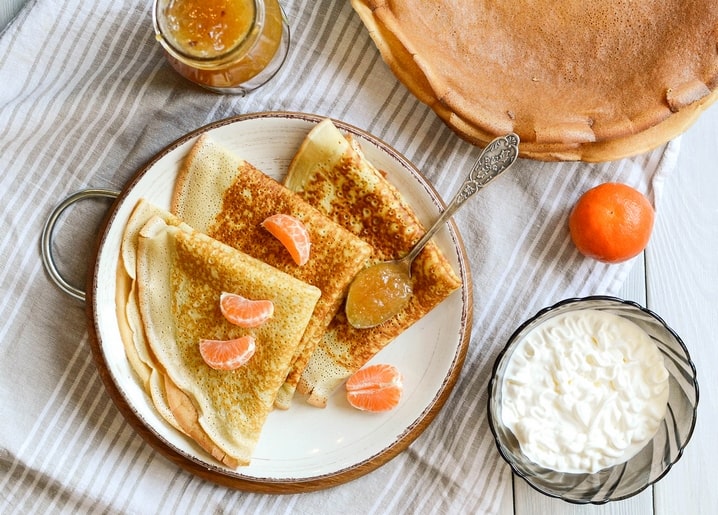 Згорнуті млинці з часточками мандарина, абрикосовим джемом і вершками на тарілці