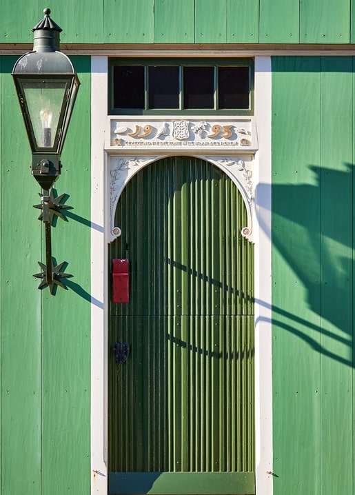 Green wooden house facade with an arched door, antique lantern, and 1895 date carving