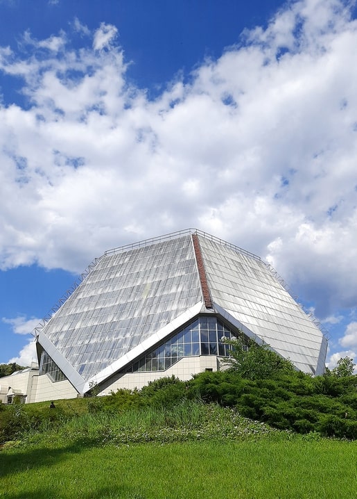 Angular glass-and-metal pyramid roof of the Hryshko Botanical Garden greenhouse against a cloudy sky
