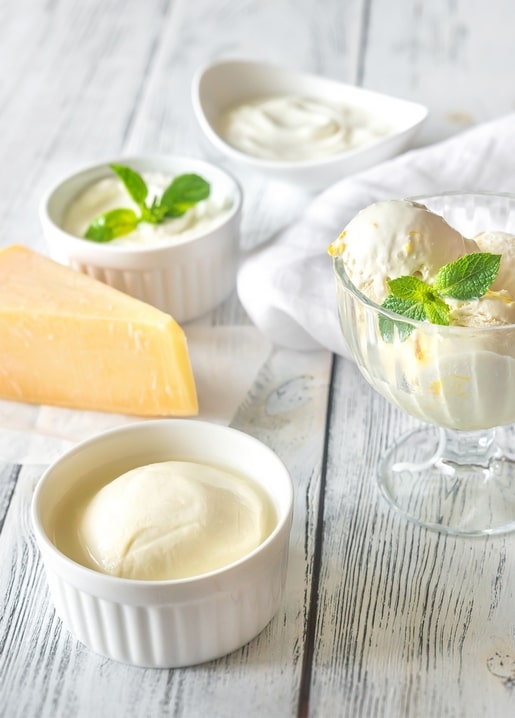 Eis im Glas mit Minze neben Schälchen Frischkäse und einem Stück Hartkäse auf weißem Holz