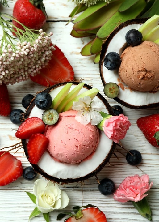 Erdbeer- und Schokoladeneis in Kokosnusshälften mit Beeren, Apfelscheiben und Blüten