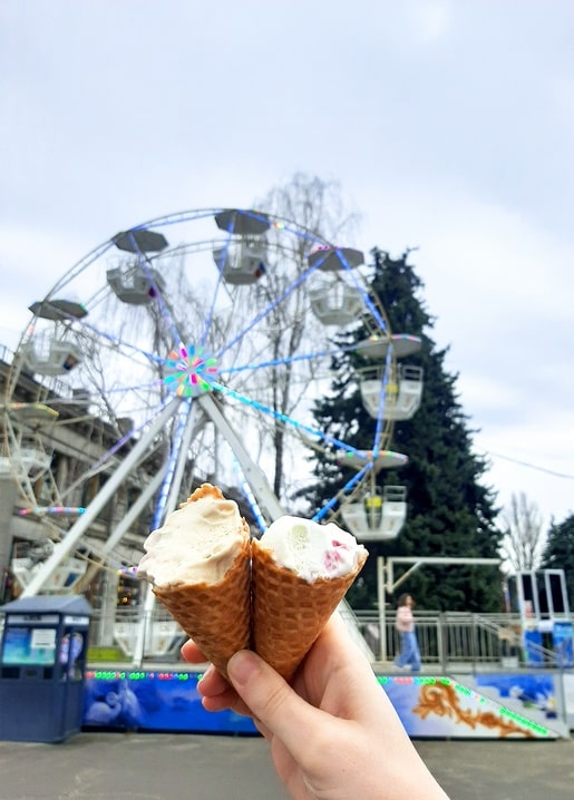Hand holding two ice cream cones in front of the VDNG Ferris wheel in spring