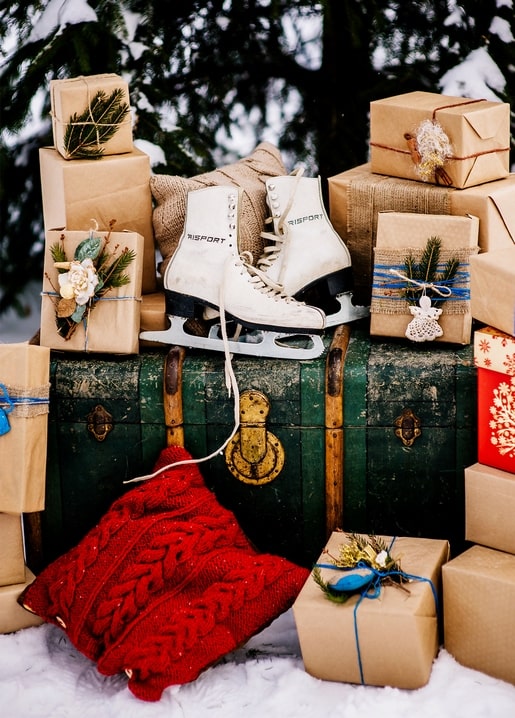 White figure skates and kraft-paper wrapped gifts on a vintage green trunk in the snow
