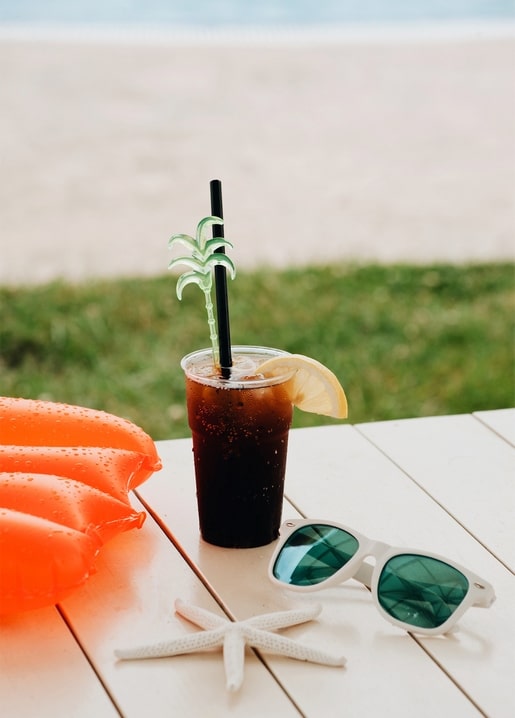 Iced cola with lemon, white sunglasses and a starfish on a beach table