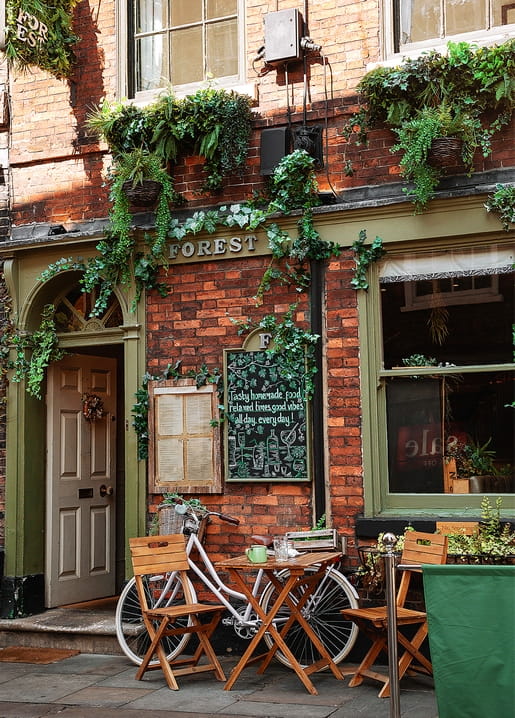 Backstein-Café-Fassade mit Efeu, Kreidetafel und Vintage-Fahrrad vor einem Bistrotisch