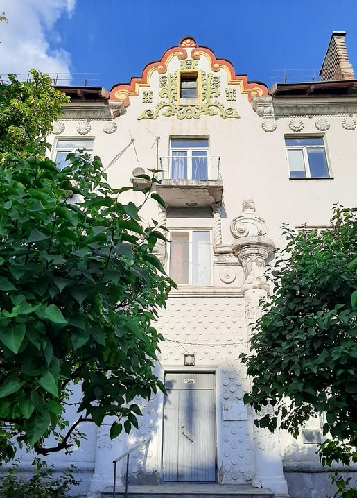 Painted coral-and-gold folk gable above a balcony on Kikvidze Street, Kyiv