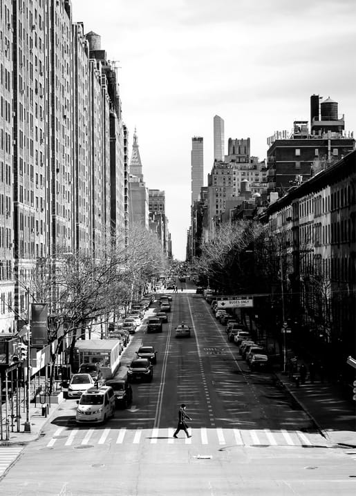 Schwarzweißfoto einer Manhattan-Straße mit Hochhäusern und einem Fußgänger