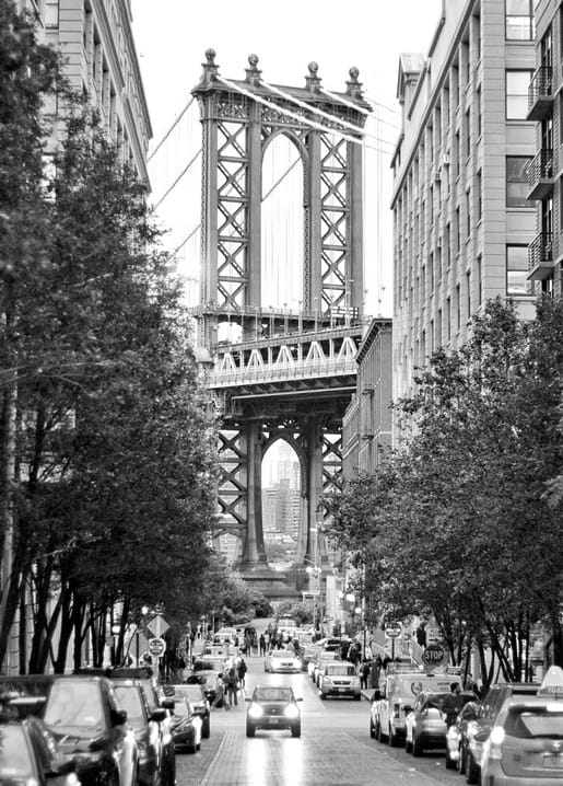 Schwarz-weißes Foto der Manhattan Bridge über einer baumgesäumten Brooklyn-Straße mit parkenden Autos