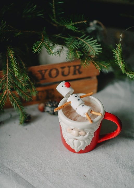 Toasted marshmallow snowman on skewers over cocoa in a red Santa-face mug