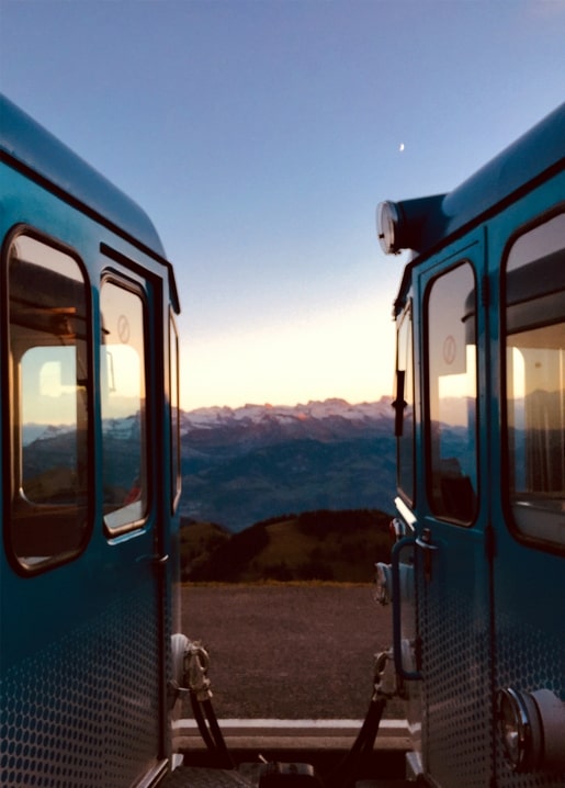 View between two mountain railway carriages at dusk with a crescent moon over peaks