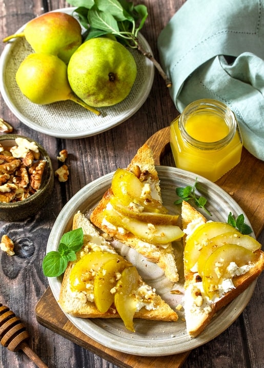 Toast with pears, cheese and walnuts beside a jar of honey and fresh pears