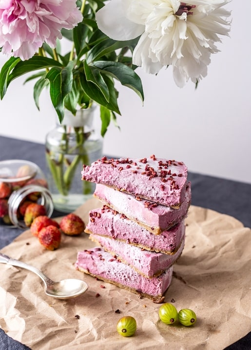 Stack of pink sorbet cake layers beside peonies, gooseberries, and strawberries on a table
