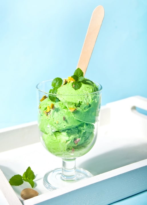 Zwei Kugeln Pistazieneis im Glas mit frischer Minze und gehackten Pistazien