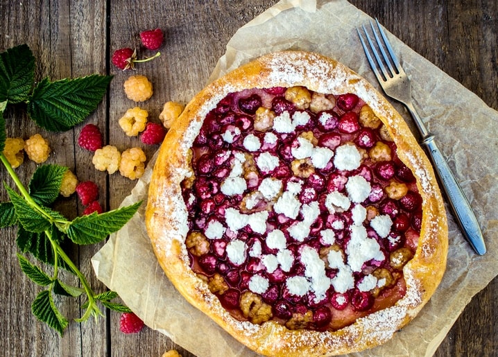 Rustic raspberry galette dusted with powdered sugar on a wooden table with a fork