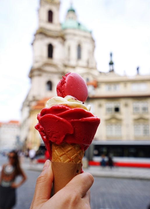 Hand hält eine Himbeersorbet-Waffel mit rosa Macaron vor einem alten Kirchturm