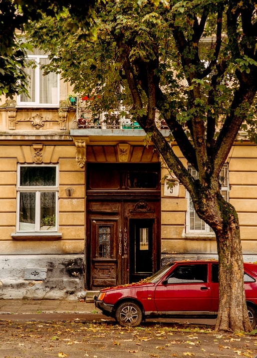 Rotes Auto unter einem Kastanienbaum vor einem alten gelben Haus in der Altstadt