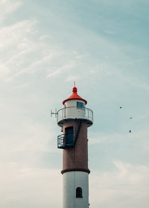 Brick and white lighthouse with a red lantern room, birds flying nearby