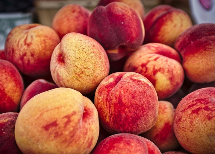 Close-up pile of ripe peaches with red-blushed, fuzzy skin