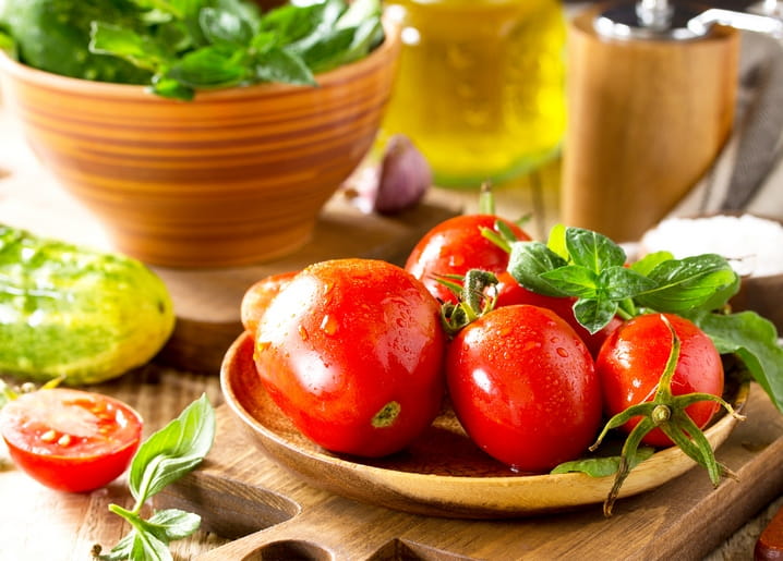Reife Tomaten mit Basilikum, Knoblauch und Olivenöl auf einem Holzbrett