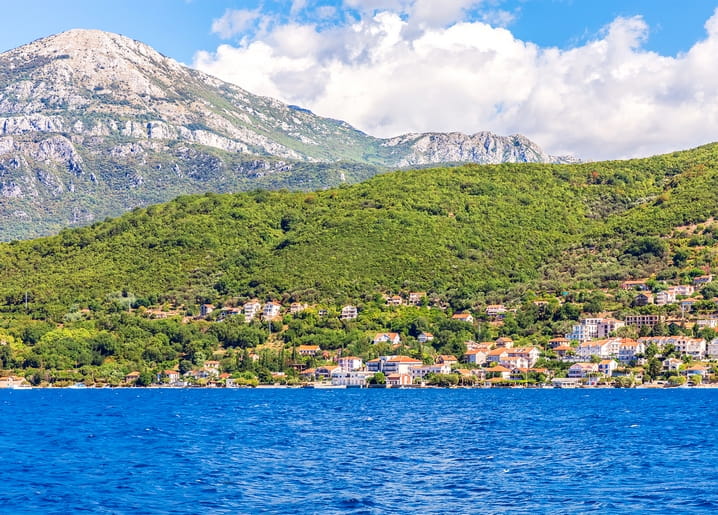 Whitewashed seaside village with red roofs beneath forested hills and mountain peaks