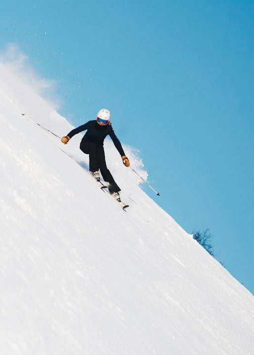 Skier carving a turn down a snowy slope under a bright blue sky