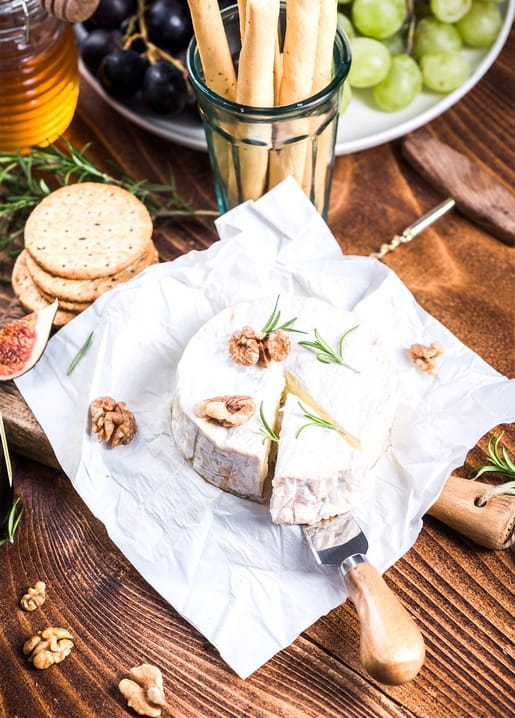 Aufgeschnittener Camembert mit Walnüssen und Rosmarin neben Crackern, Trauben und Honig