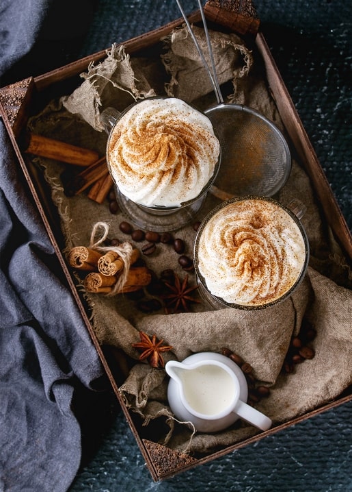 Zwei Gläser Latte mit Schlagsahne und Zimt im Holztablett