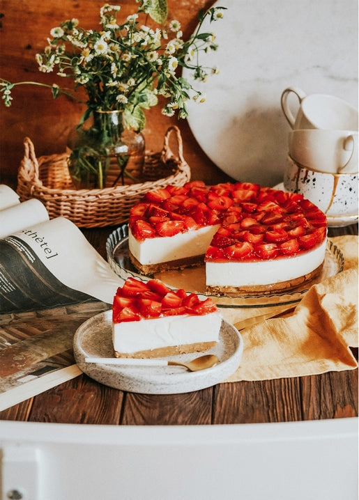 Strawberry cheesecake with a cut slice, fresh daisies and vintage teacups on a table
