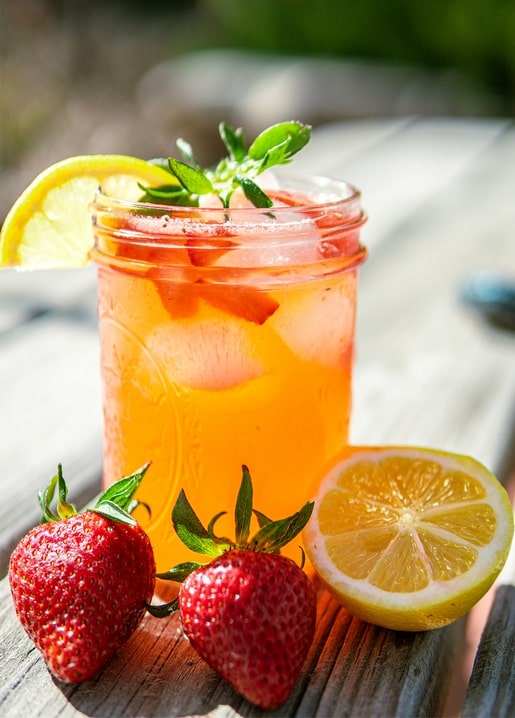 Einmachglas mit Erdbeer-Limonade, Zitrone und Minze neben frischen Erdbeeren
