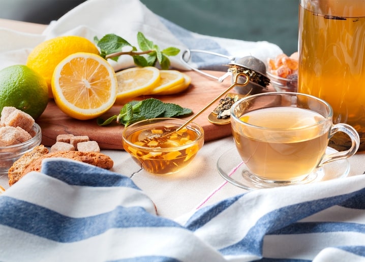 Glass cup of tea with lemon slices, honey and mint on a striped cloth